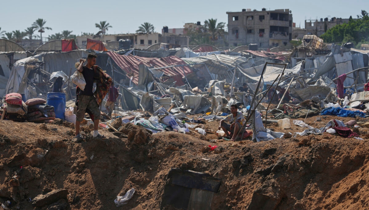 A Palestinian walks on the edge of a crater after Israeli military strikes in a tent camp for displaced people near Al-Aqsa Hospital, in Deir al-Balah, Thursday, Aug. 21, 2025. (AP Photo/Jehad Alshrafi)